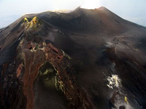 Figura 4 – Visione aerea, da Est, dell’area sommitale dell’Etna. A sinistra, si nota il cono del Cratere di Sud-Est, “bucato” in corrispondenza della sua base orientale dalla bocca eruttiva che costruirà, dal 2011 in poi, il Nuovo Cratere di Sud-Est. A destra, si osserva la frattura eruttiva che ha alimentato l’eruzione laterale del 2008-2009. Foto: Marco Neri.